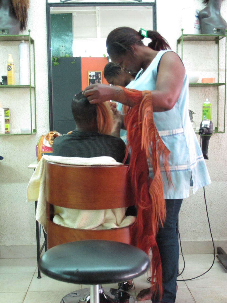 Die Friseurin klebt hier das Kunsthaar Strähne für Strähne unter das natürliche Haar, am Ende schneidet sie es zur Frisur.